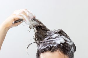 A girl washes her hair with shampoo on white background, front view
